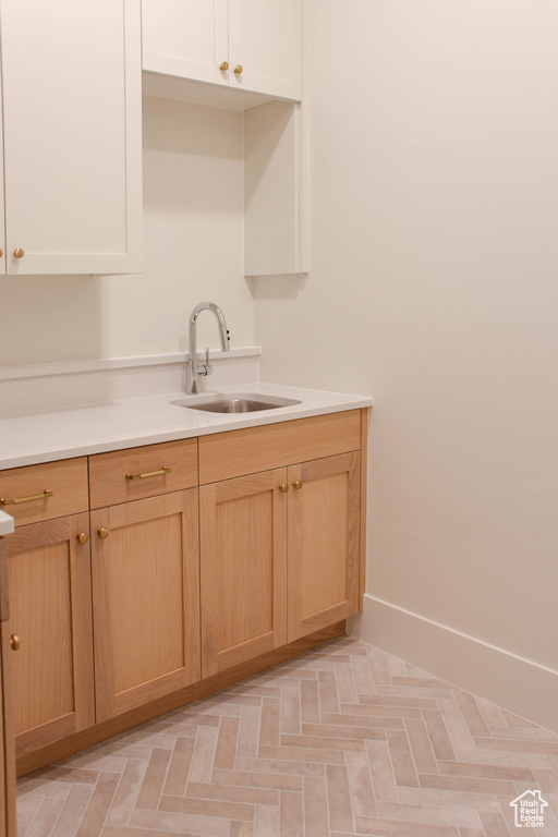 Kitchen with a sink, light countertops, light brown cabinets, and baseboards