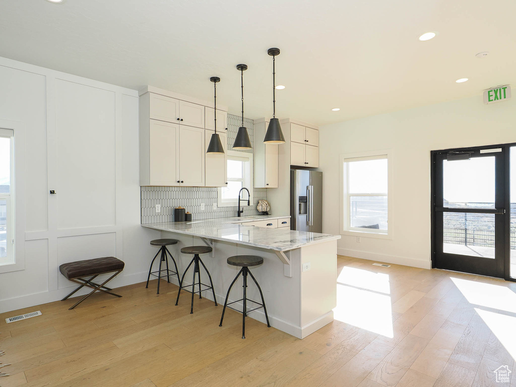 Kitchen featuring stainless steel refrigerator with ice dispenser, light wood-type flooring, a breakfast bar area, a peninsula, and light stone countertops