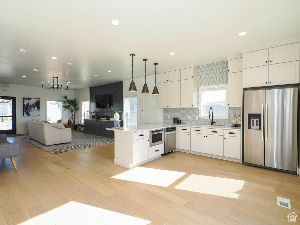Kitchen featuring appliances with stainless steel finishes, open floor plan, light wood-style flooring, tasteful backsplash, and recessed lighting