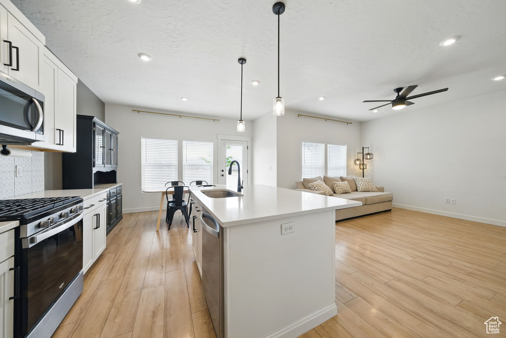 Kitchen with appliances with stainless steel finishes, a sink, a ceiling fan, light wood-style flooring, and tasteful backsplash