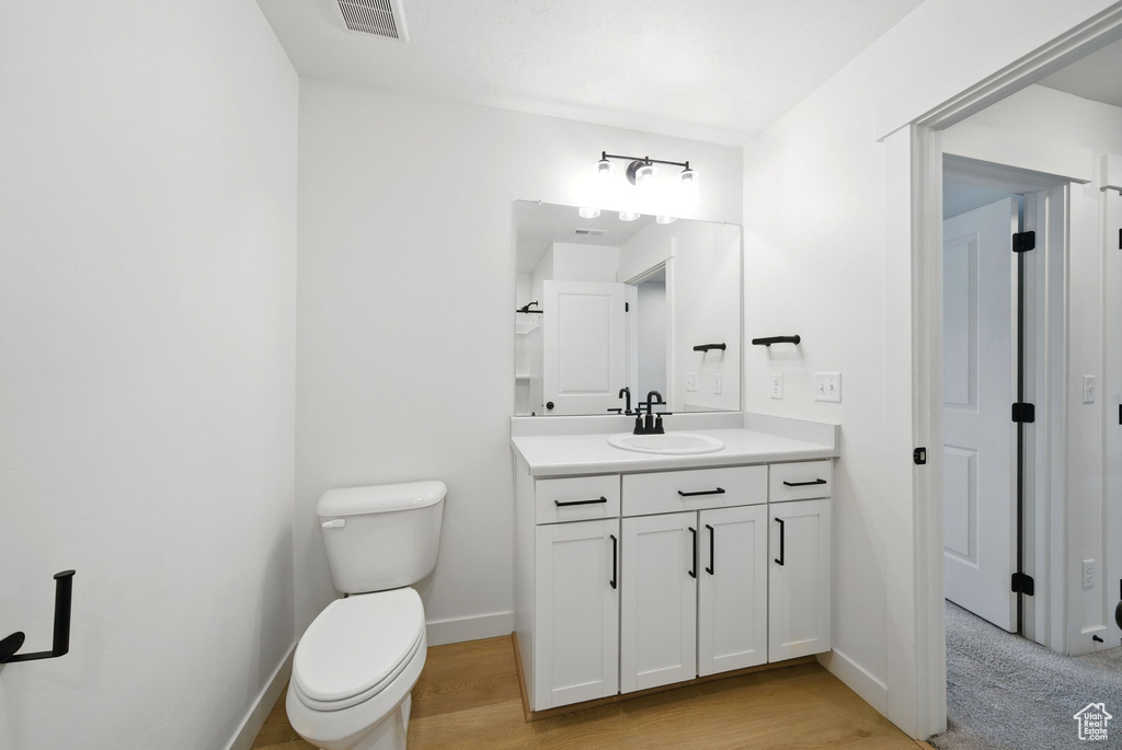 Bathroom featuring toilet, vanity, baseboards, and wood finished floors