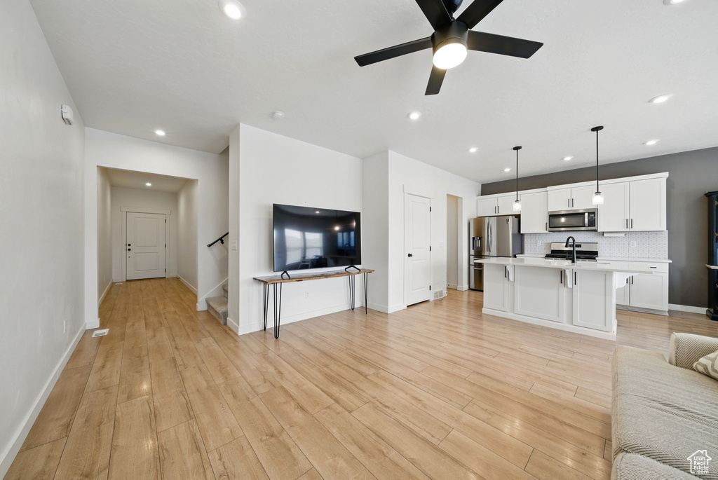 Unfurnished living room featuring a sink, light wood-style floors, ceiling fan, stairs, and recessed lighting