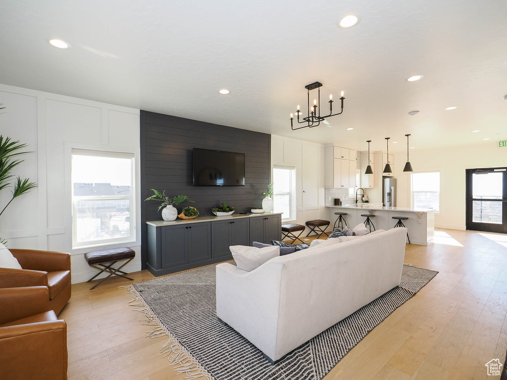 Living room with light wood-style flooring, recessed lighting, a chandelier, and a decorative wall