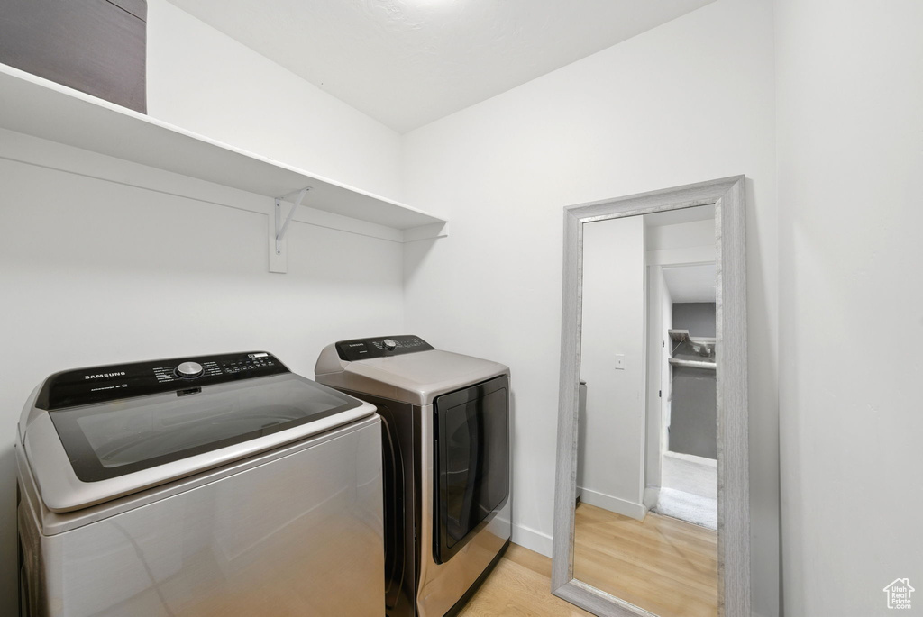 Clothes washing area featuring light wood finished floors, washer and clothes dryer, and baseboards