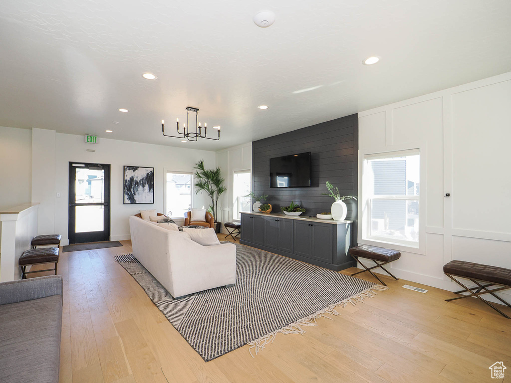 Living room featuring light wood-style floors, a decorative wall, recessed lighting, and a chandelier