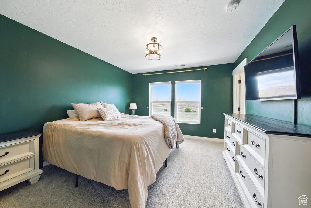Bedroom featuring light carpet, a chandelier, baseboards, and a textured ceiling