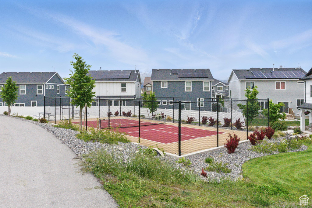 View of tennis court with a residential view and fence