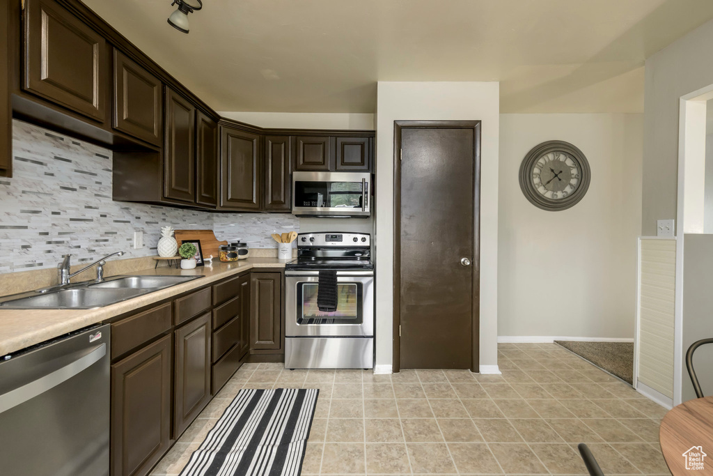 Kitchen featuring stainless steel appliances, a sink, dark brown cabinetry, tasteful backsplash, and light countertops