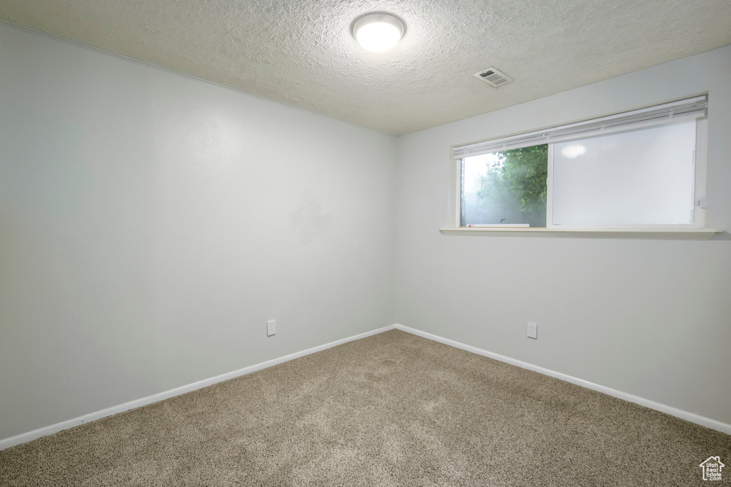 Carpeted empty room with a textured ceiling and baseboards