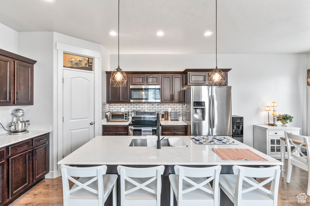 Kitchen featuring stainless steel appliances, a sink, light wood-style floors, dark brown cabinets, and recessed lighting