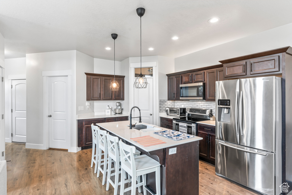 Kitchen with appliances with stainless steel finishes, a sink, dark brown cabinets, a center island with sink, and light countertops