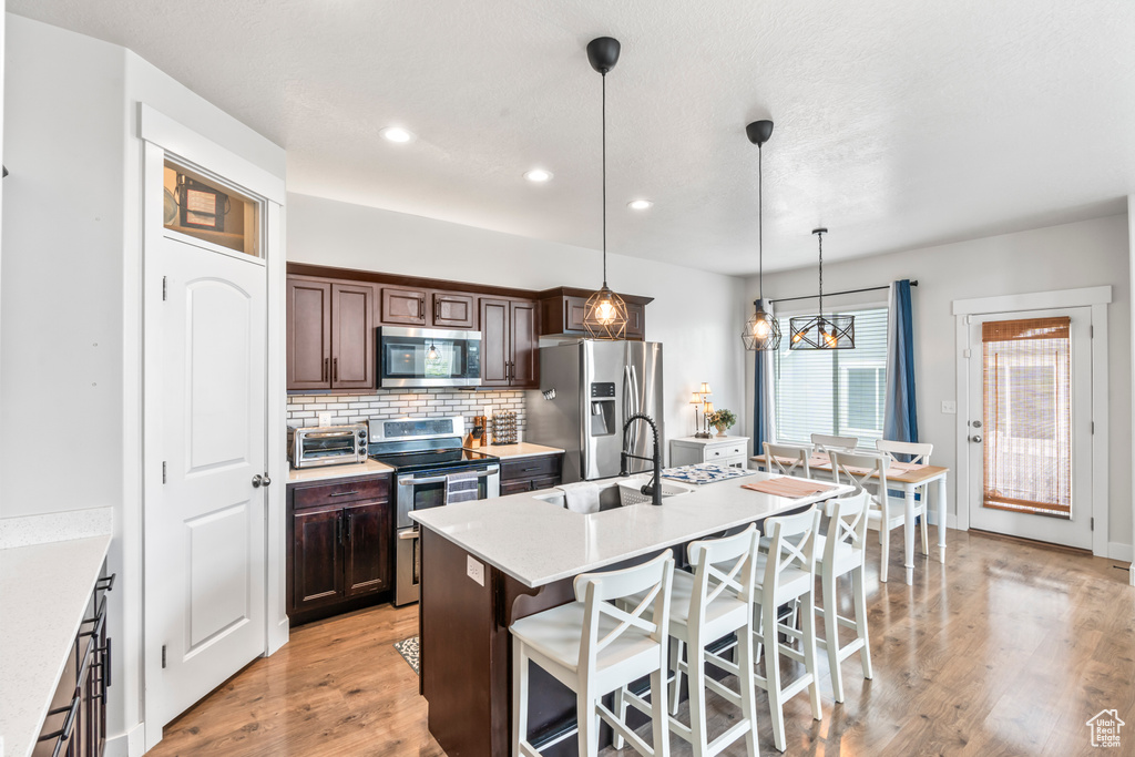 Kitchen with appliances with stainless steel finishes, a sink, a breakfast bar area, decorative backsplash, and light countertops