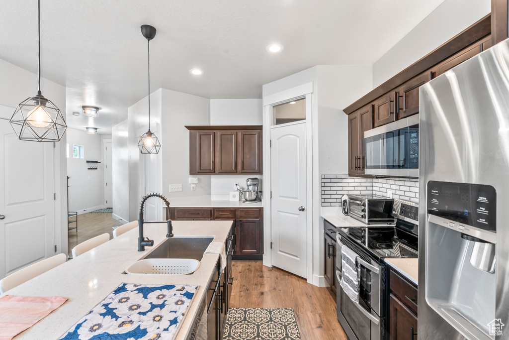 Kitchen featuring appliances with stainless steel finishes, a sink, decorative light fixtures, dark brown cabinetry, and light wood-type flooring