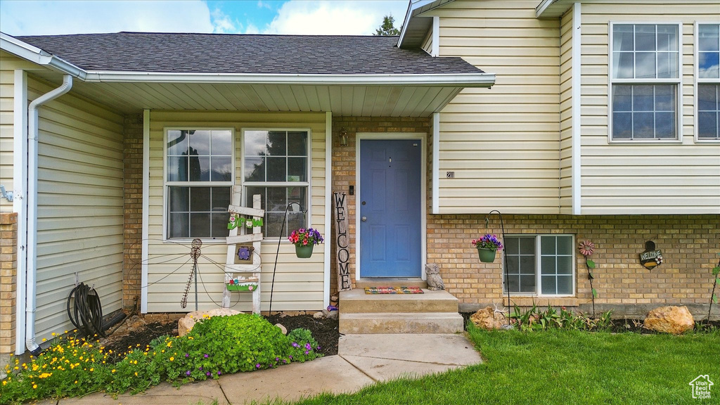 Doorway to property with a shingled roof, a yard, and brick siding
