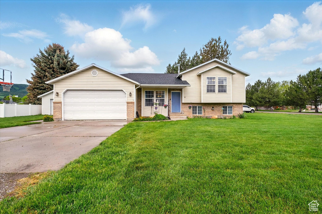 Tri-level home with brick siding, an attached garage, driveway, and a shingled roof