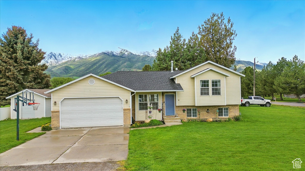Split level home with a mountain view, brick siding, a front lawn, and an attached garage