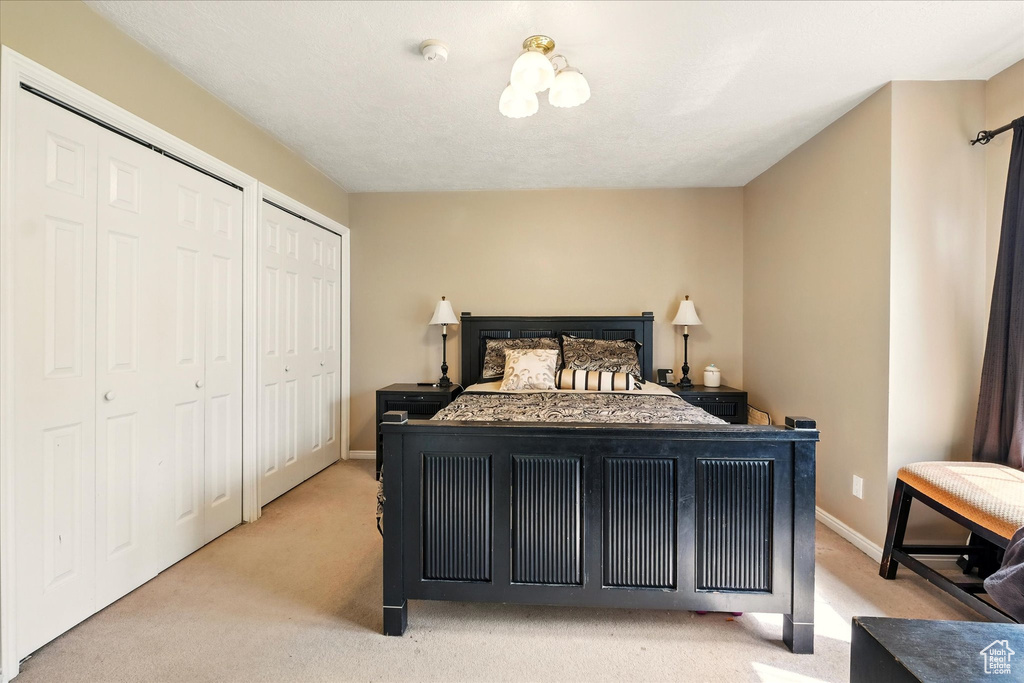 Bedroom featuring light carpet, two closets, and baseboards