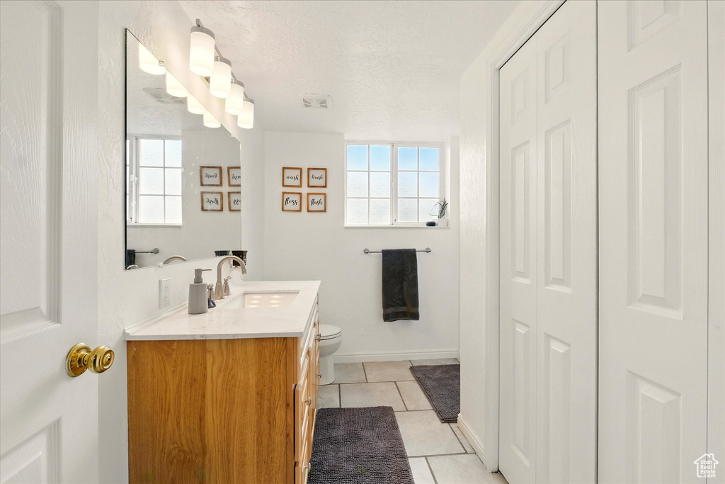 Bathroom with tile patterned floors, toilet, vanity, a closet, and a textured ceiling