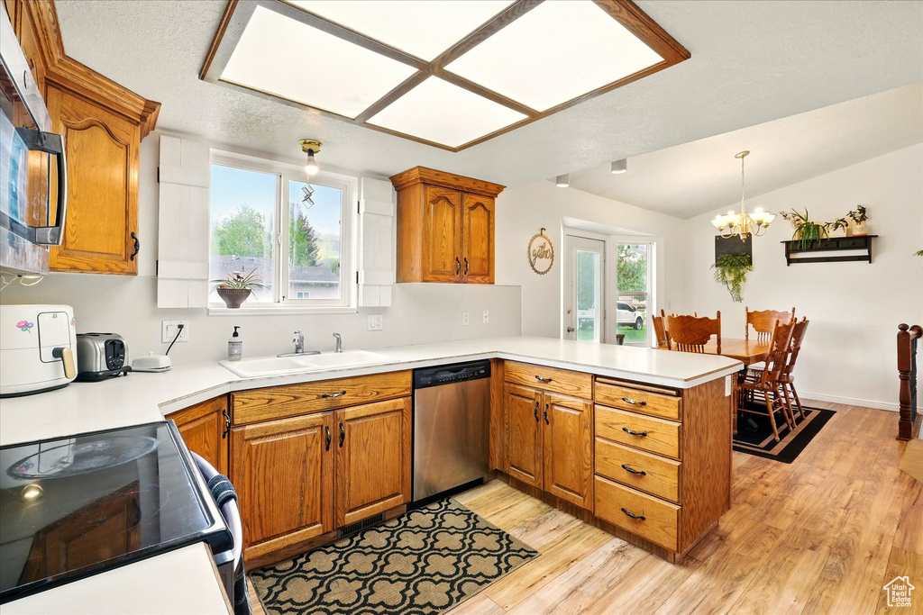 Kitchen featuring appliances with stainless steel finishes, a sink, a peninsula, light wood-style flooring, and lofted ceiling