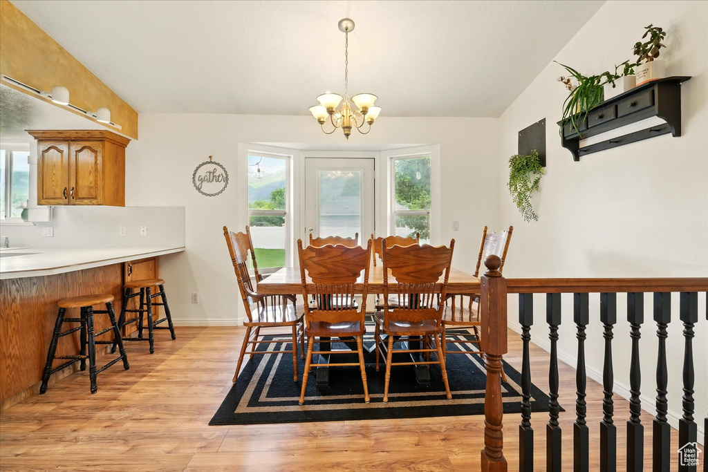 Dining space with light wood-style floors, a chandelier, vaulted ceiling, and baseboards