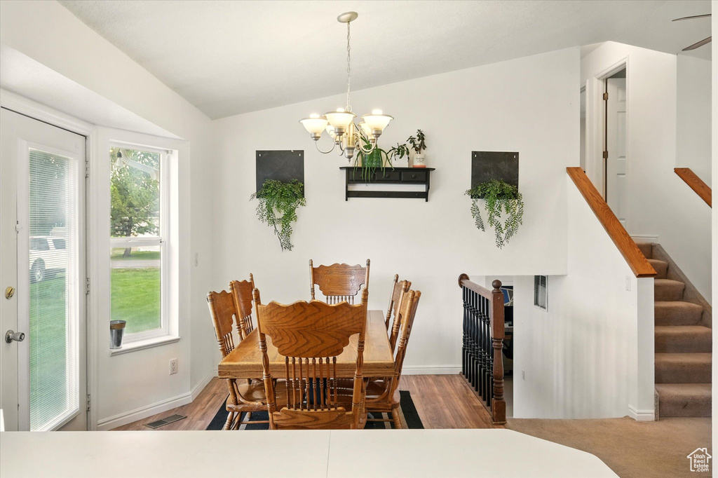 Dining room with a chandelier, wood finished floors, baseboards, stairway, and lofted ceiling