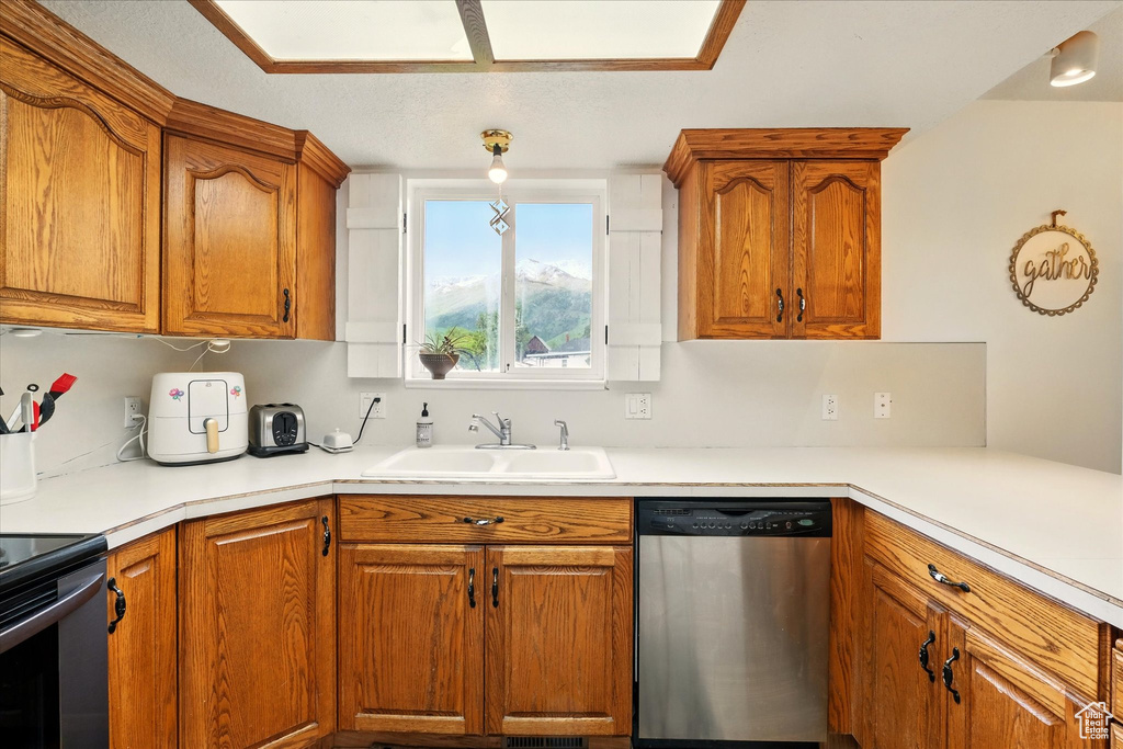Kitchen featuring dishwasher, a sink, brown cabinetry, and light countertops
