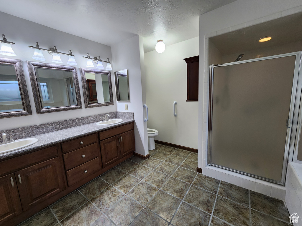 Bathroom featuring a shower stall, double vanity, toilet, and baseboards