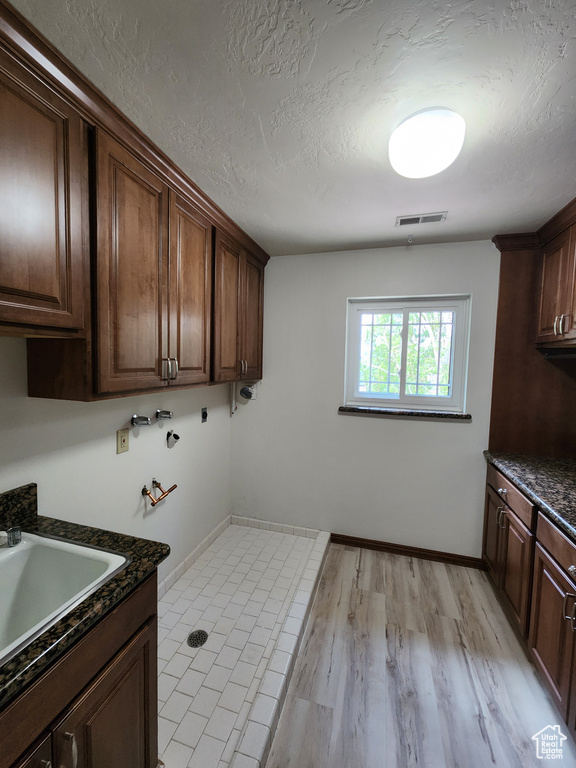 Laundry area with cabinet space, hookup for a washing machine, a textured ceiling, baseboards, and light wood-style flooring