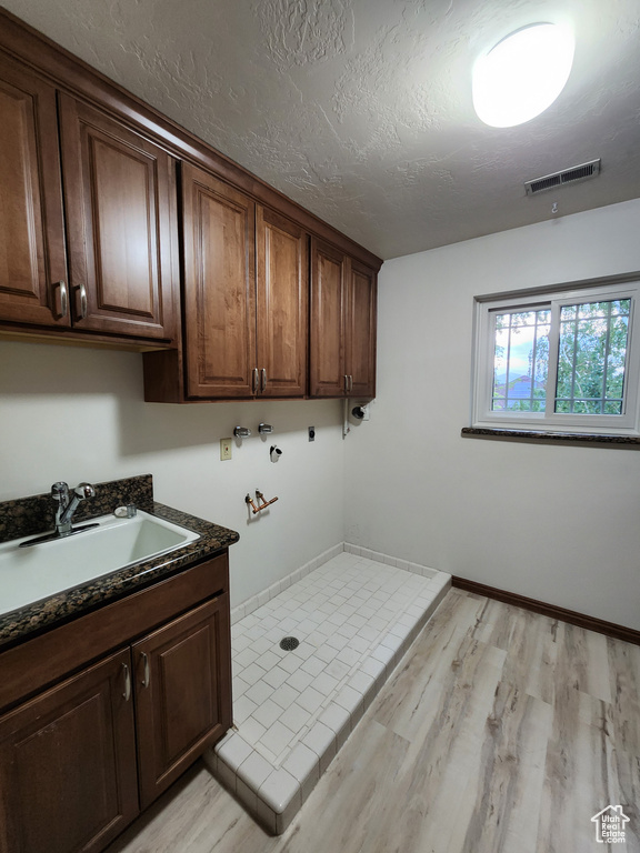 Laundry area with cabinet space, light wood finished floors, hookup for a washing machine, a textured ceiling, and baseboards