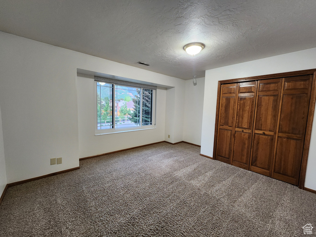 Unfurnished bedroom with carpet, baseboards, a textured ceiling, and a closet