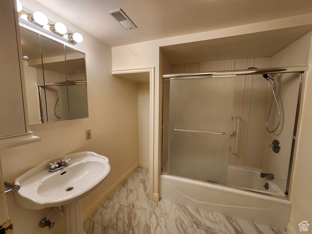 Bathroom with marble look tiles, a sink, combined bath / shower with glass door, and baseboards