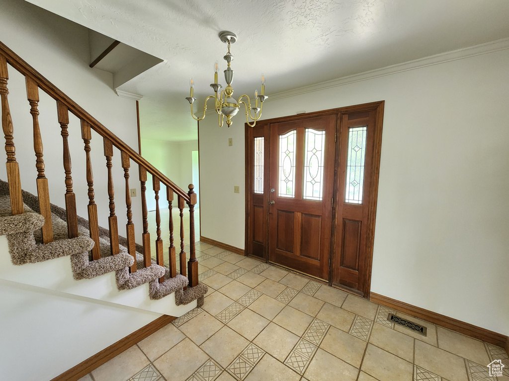 Foyer with baseboards, a chandelier, stairs, and crown molding