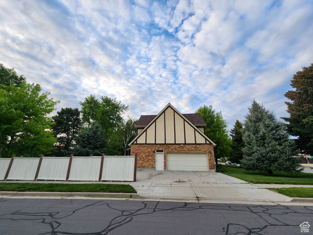 Tudor-style house with brick siding, concrete driveway, fence, and a garage
