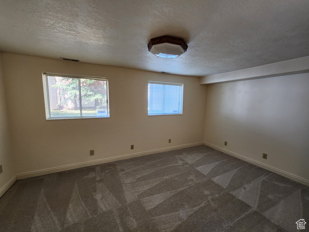 Empty room featuring a textured ceiling, carpet floors, and baseboards