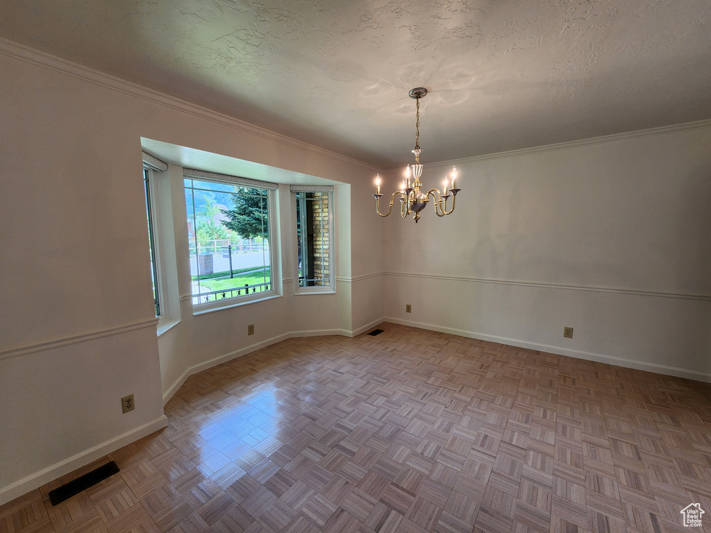Empty room with a chandelier, baseboards, and ornamental molding