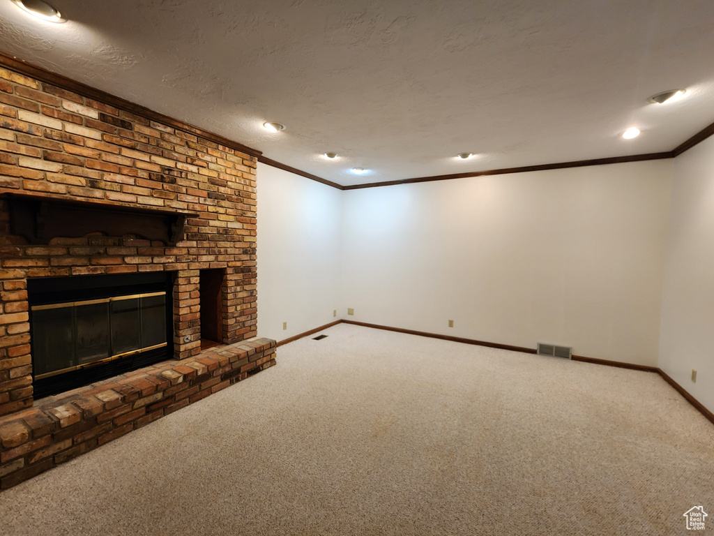 Unfurnished living room with carpet, ornamental molding, baseboards, and a brick fireplace