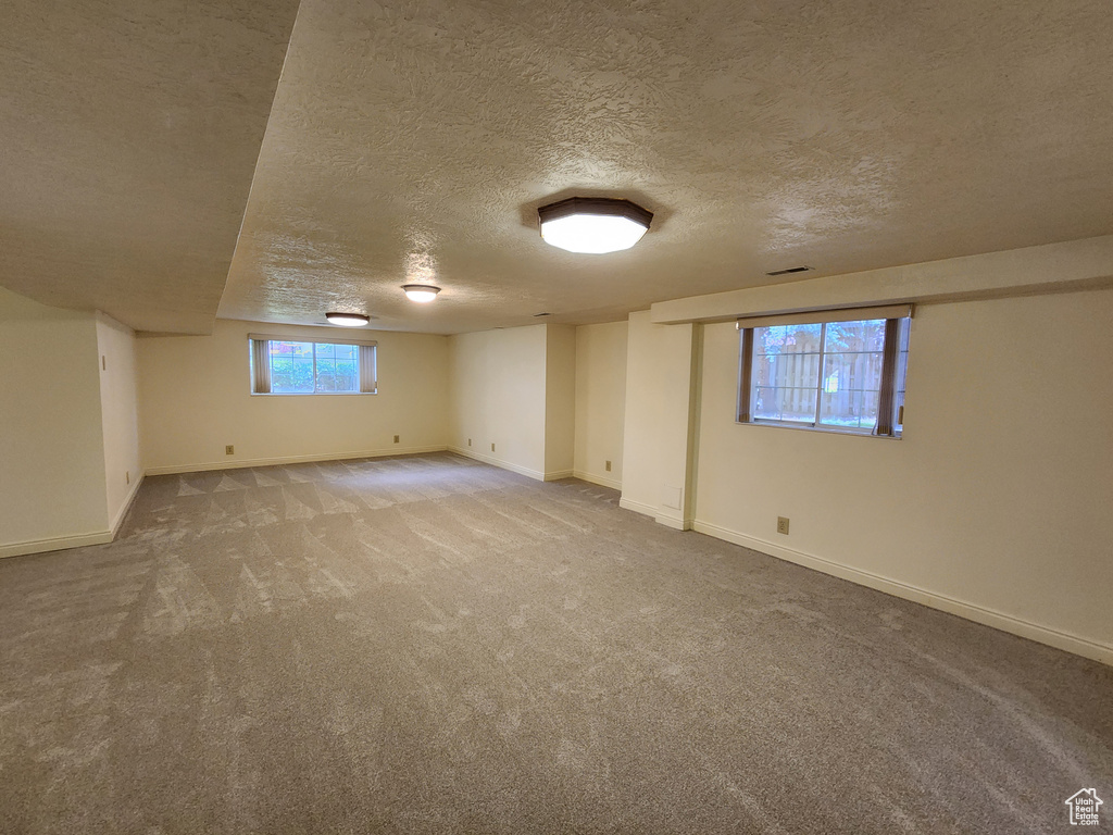 Below grade area featuring a textured ceiling, carpet flooring, and baseboards