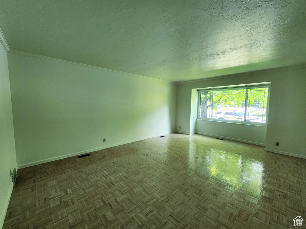 Empty room featuring baseboards, a textured ceiling, and crown molding