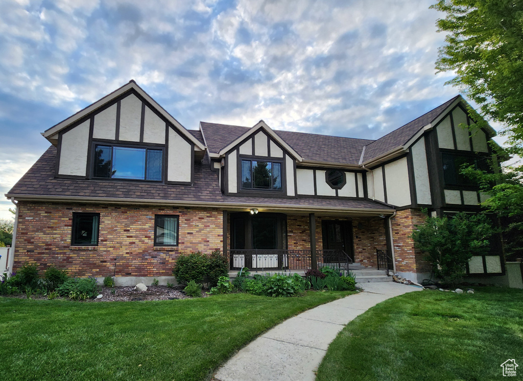 Tudor house featuring covered porch, stucco siding, a front lawn, and brick siding
