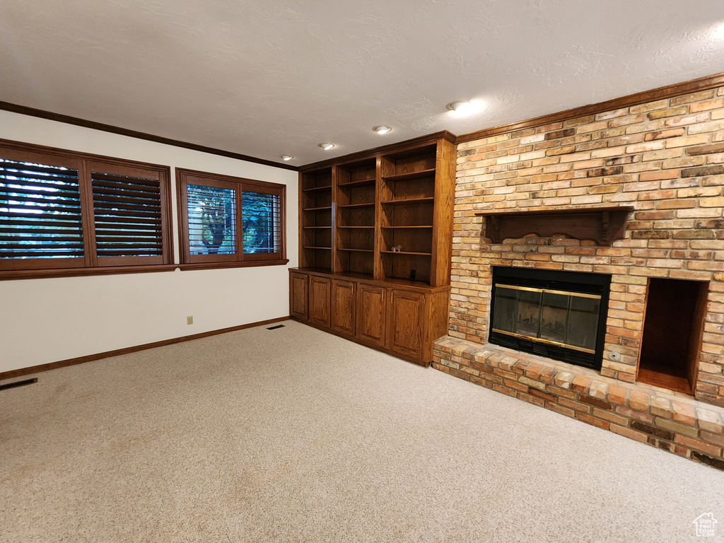 Unfurnished living room featuring carpet, baseboards, a brick fireplace, crown molding, and a textured ceiling