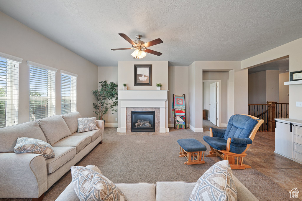 Living area with a ceiling fan, baseboards, a glass covered fireplace, a textured ceiling, and carpet floors