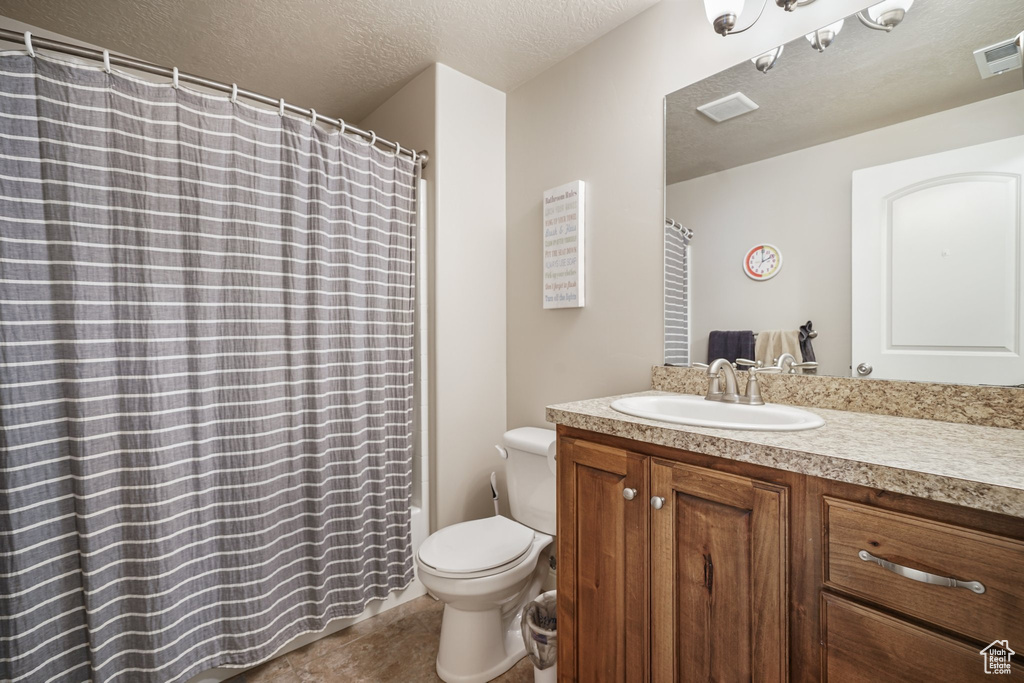 Bathroom featuring vanity, toilet, a textured ceiling, a shower with shower curtain, and tile patterned floors