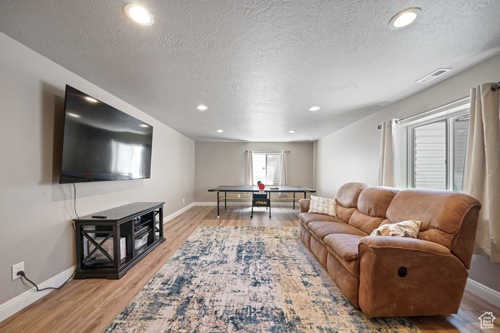 Living area featuring a textured ceiling, baseboards, light wood-type flooring, and recessed lighting