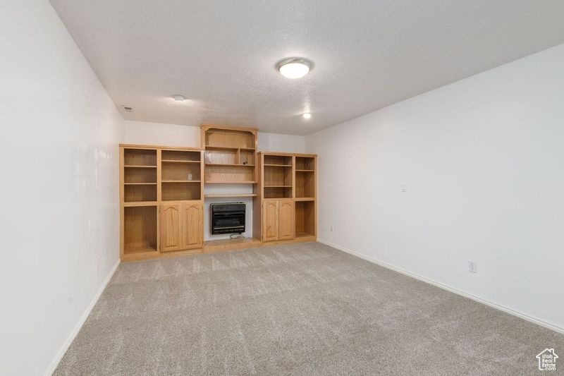 Unfurnished living room with heating unit, baseboards, light carpet, and a textured ceiling