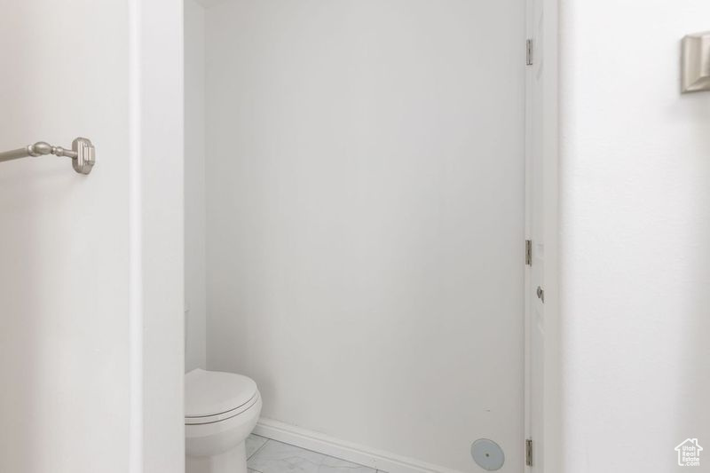 Bathroom with toilet, marble finish floors, and baseboards