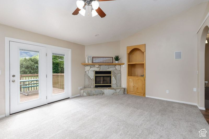 Unfurnished living room with a ceiling fan, arched walkways, baseboards, a fireplace, and carpet