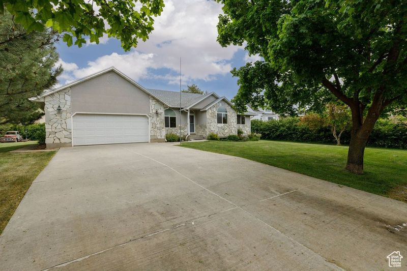 Ranch-style home with stone siding, driveway, a garage, and a front yard