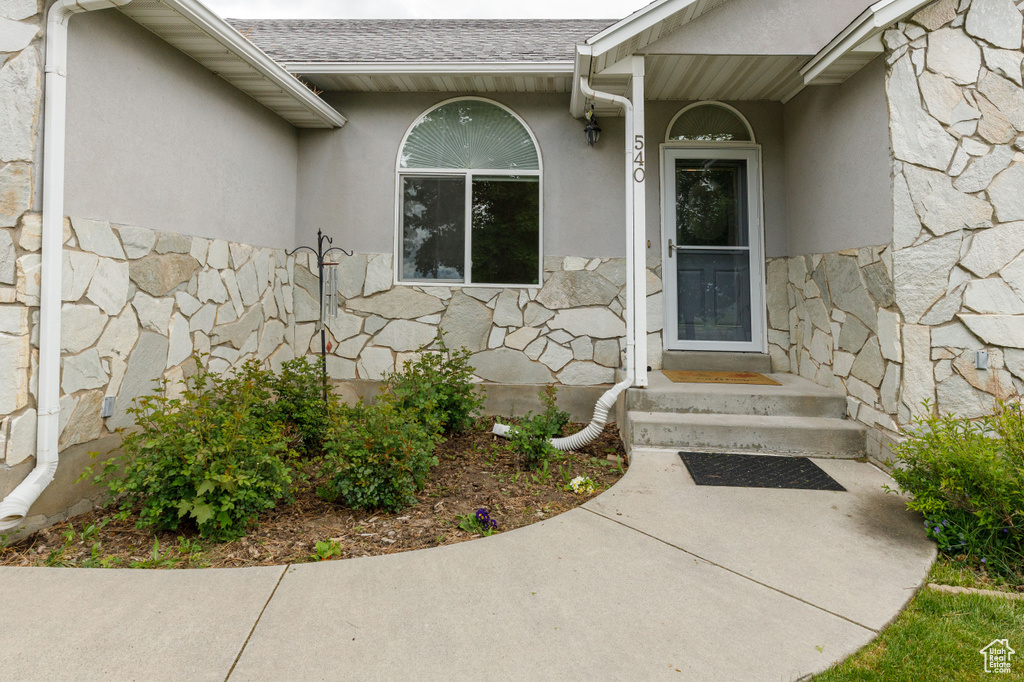 Doorway to property with stone siding, stucco siding, and a shingled roof
