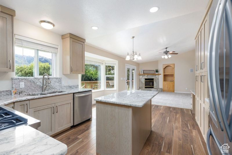 Kitchen featuring appliances with stainless steel finishes, a sink, open floor plan, a ceiling fan, and a glass covered fireplace