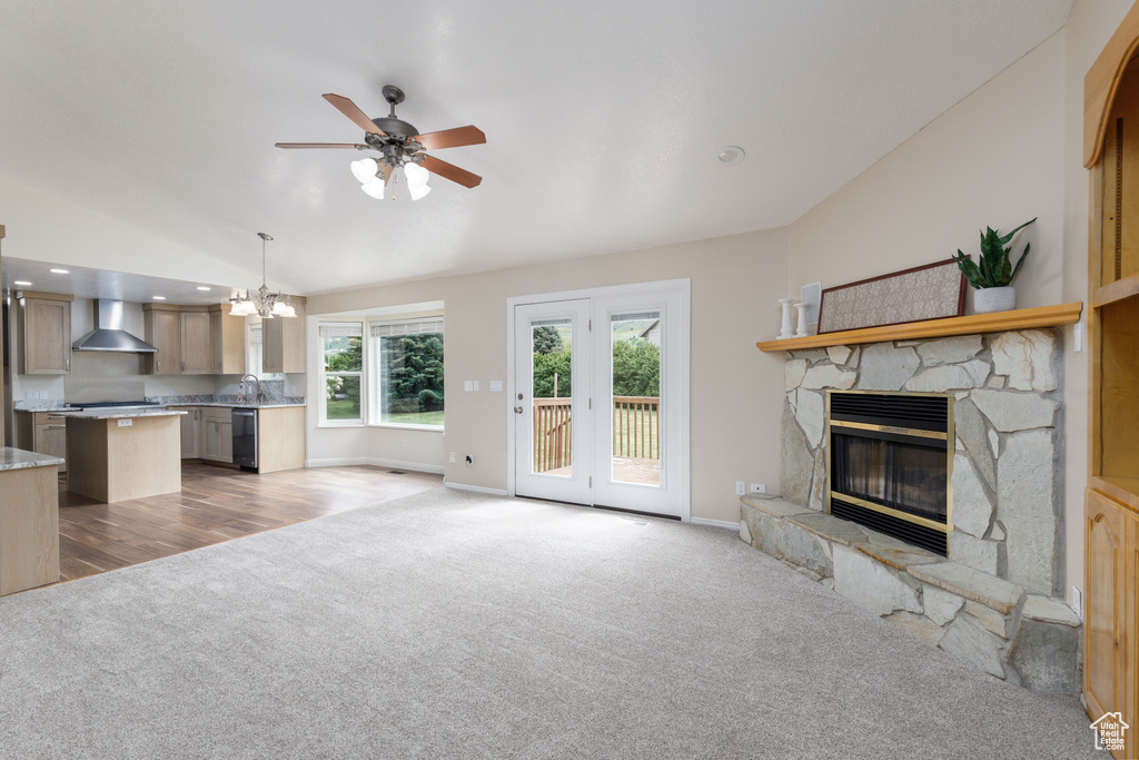 Unfurnished living room featuring light carpet, a chandelier, lofted ceiling, a fireplace, and ceiling fan